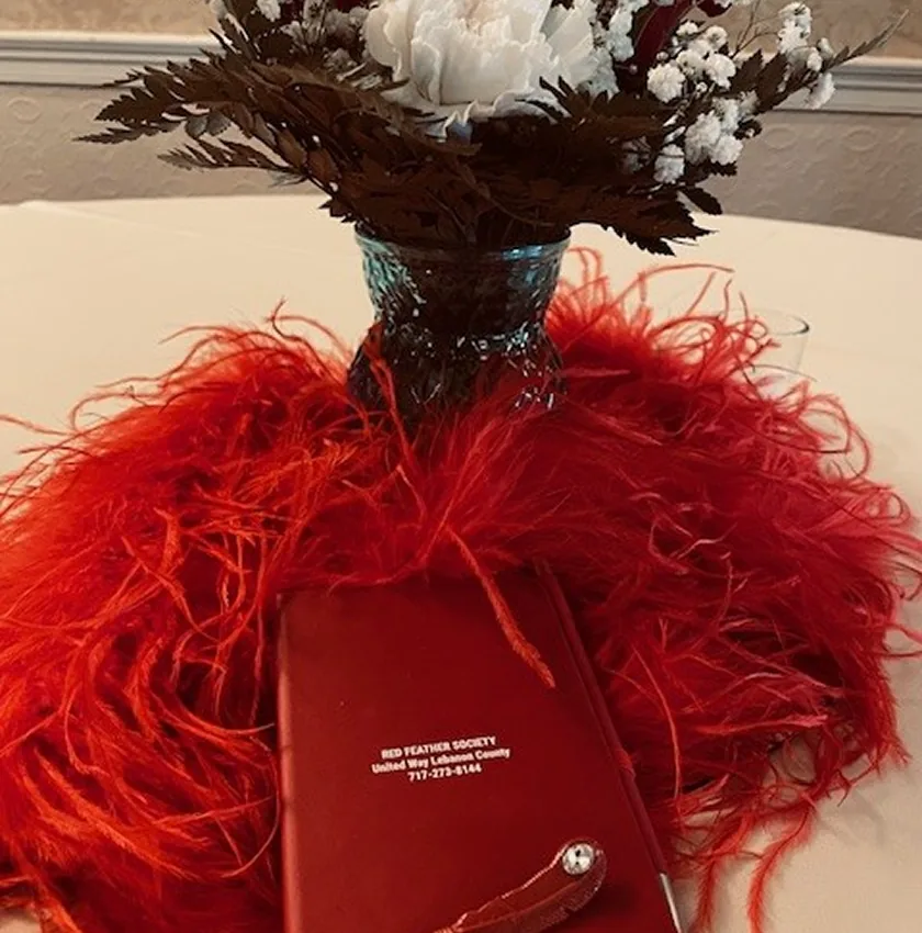 Falconer’s Guild celebration centerpiece: red feathers, book, and dark floral vase.